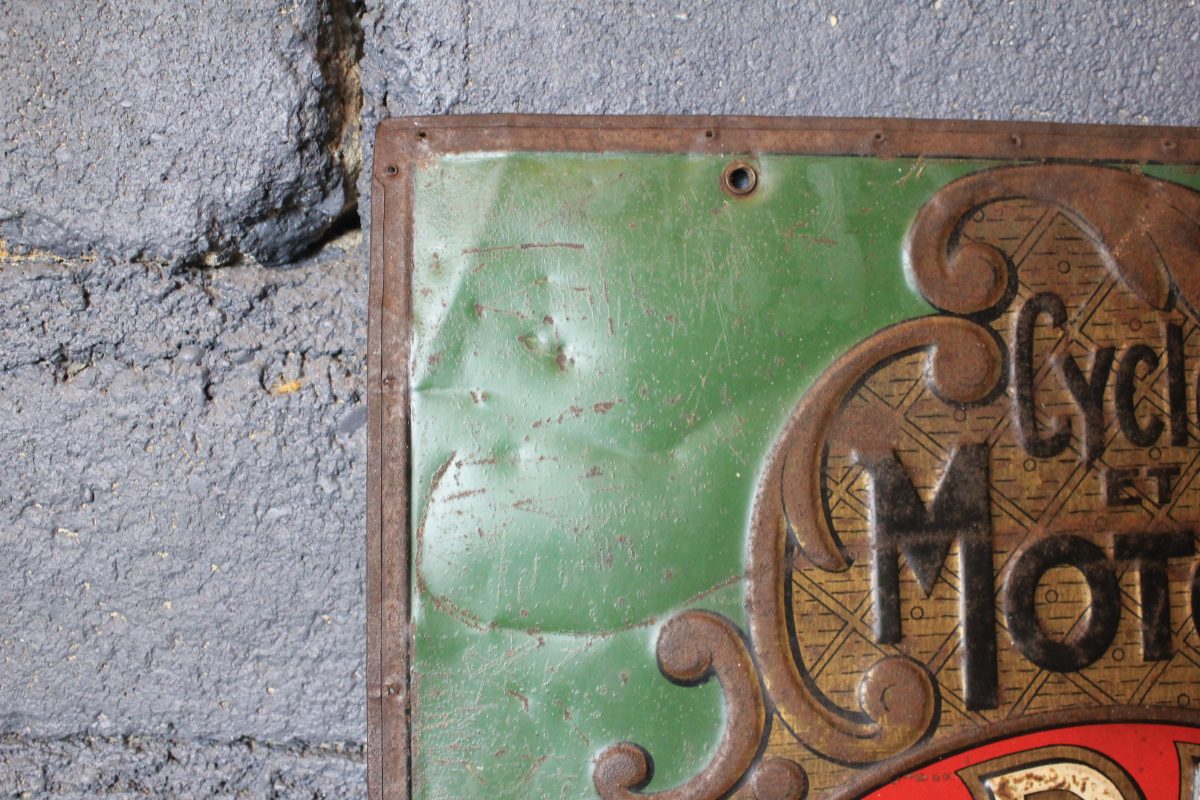 Tôle emboutie publicitaire vintage RADIOR aperçu du coin supérieur gauche de la seconde face avec le début de l'inscription de cycles et motos