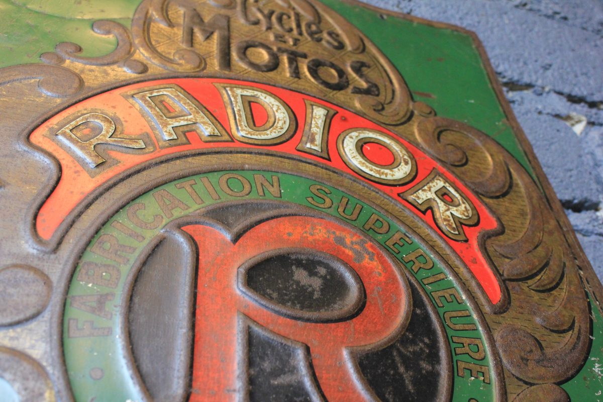 Tôle emboutie publicitaire vintage RADIOR aperçu du centre de la tôle avec le nom de la marque RADIOR bien visible ainsi que le logo et le texte cycles et motos