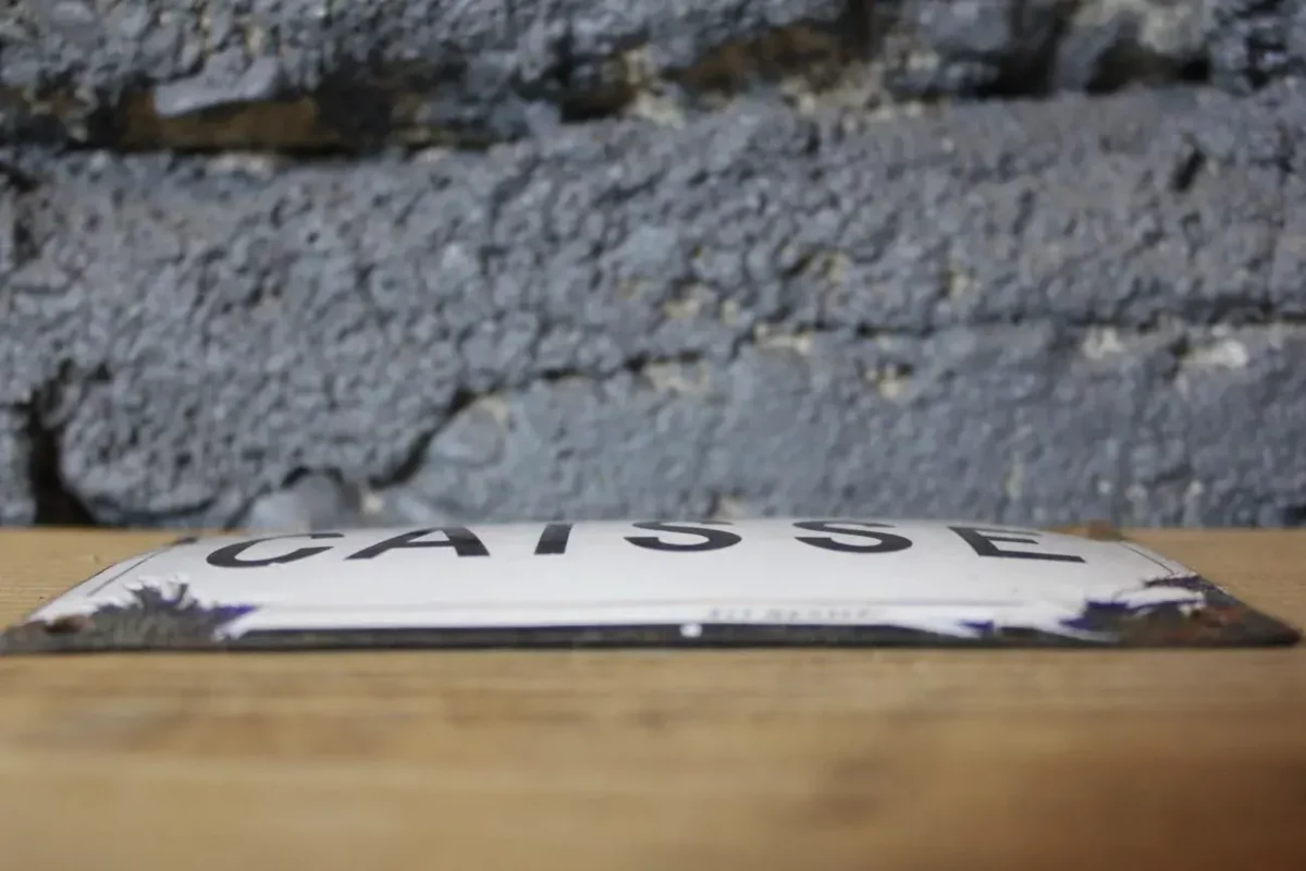 Gros plan sur l'inscription "CAISSE" de la plaque émaillée.